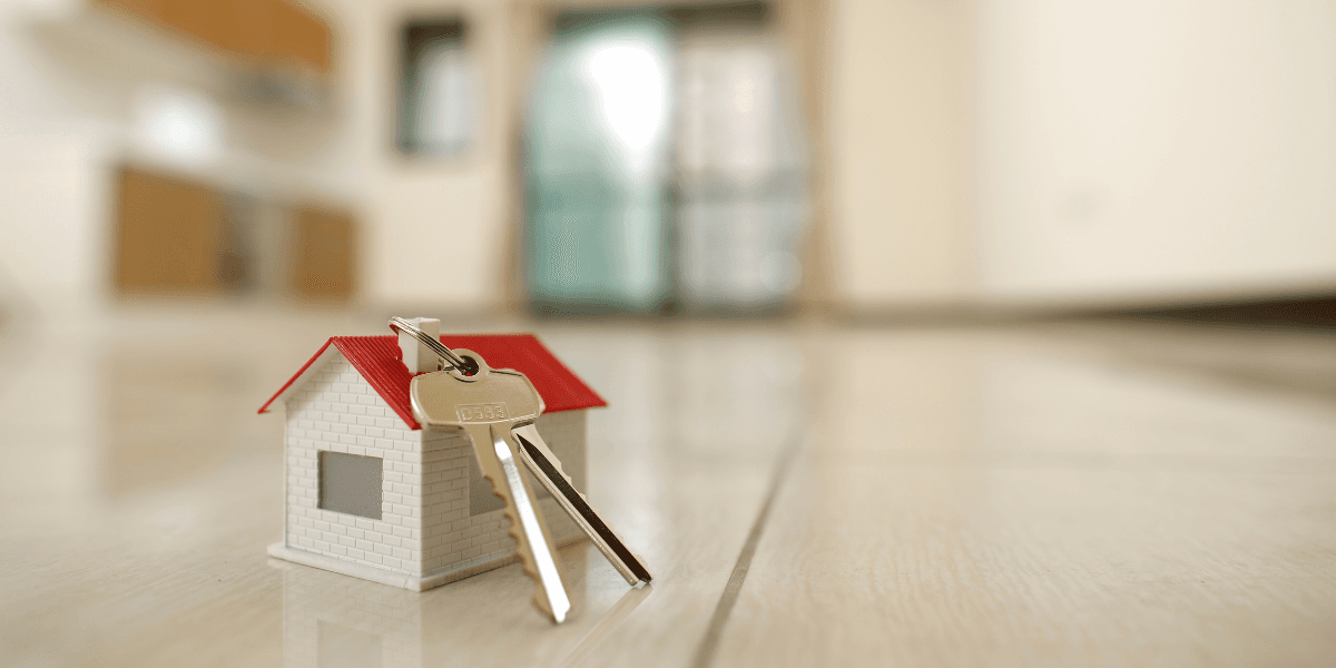 Small model house with keys placed on a wooden floor in a bright room
