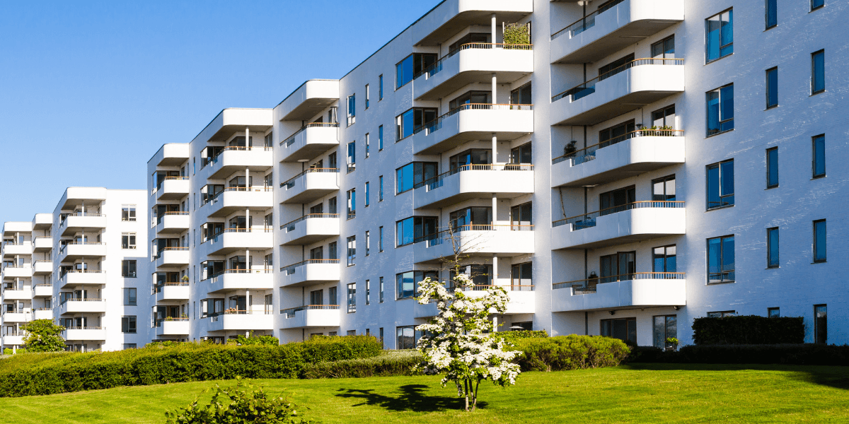 Modern residential building with balconies, green lawn, and clear blue sky
