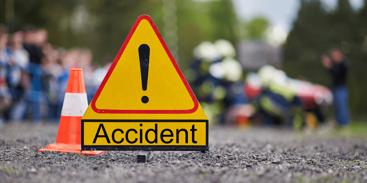 Yellow caution sign indicating an accident with blurred emergency responders in the background