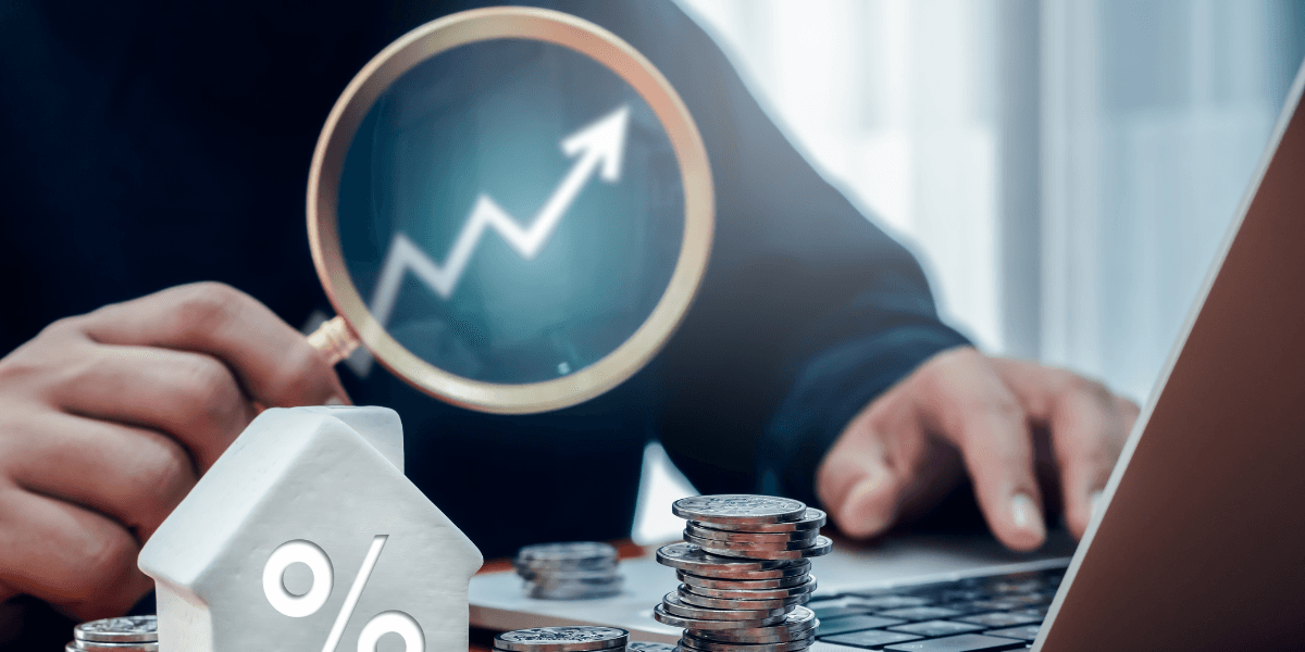 Person examining a rising graph with a magnifying glass, coins and a house figure nearby