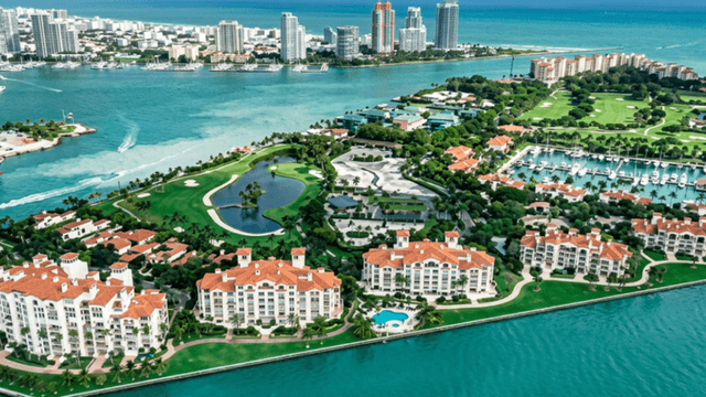 Aerial view of waterfront residences, golf courses, marina, and surrounding turquoise waters on Fisher Island.