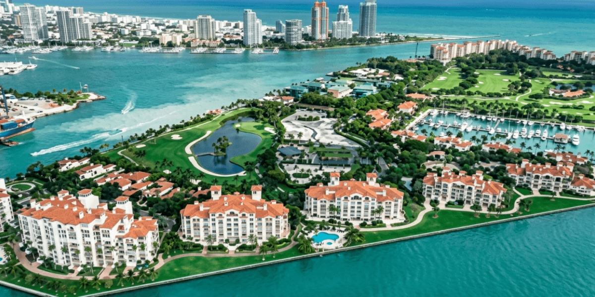 Aerial view of waterfront residences, golf courses, marina, and surrounding turquoise waters on Fisher Island.