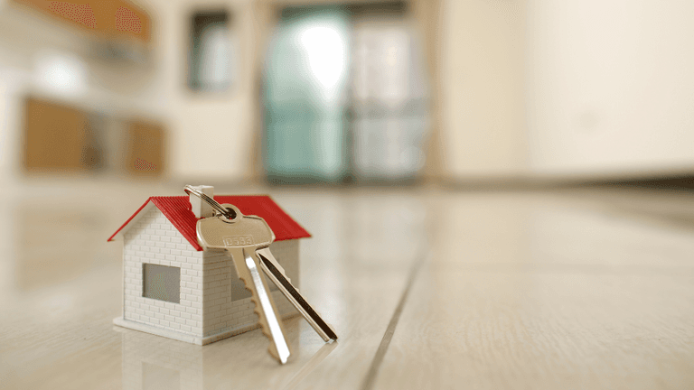 Small model house with keys placed on a wooden floor in a bright room