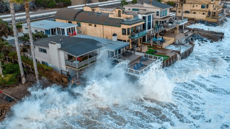 Waves crashing against coastal homes, showing erosion and power of the ocean