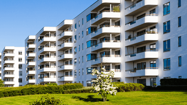 Modern residential building with balconies, green lawn, and clear blue sky