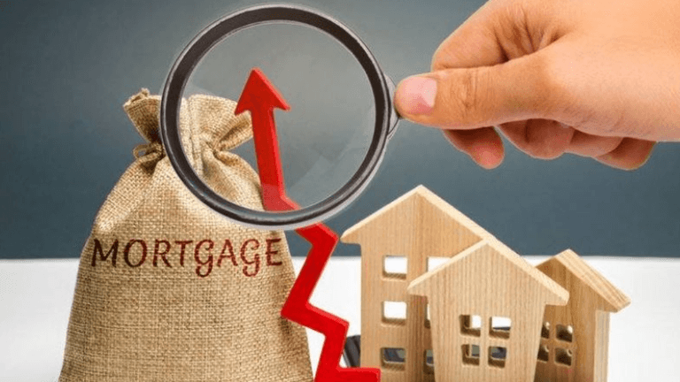 Hand holding a magnifying glass over a mortgage bag and wooden houses with a rising graph