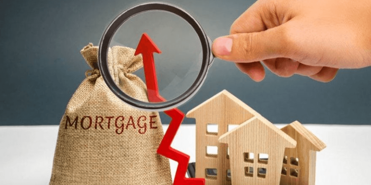 Hand holding a magnifying glass over a mortgage bag and wooden houses with a rising graph
