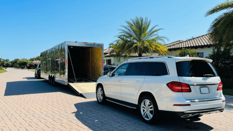 White SUV parked beside a large trailer on a sunny residential street
