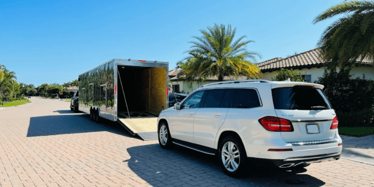 White SUV parked beside a large trailer on a sunny residential street