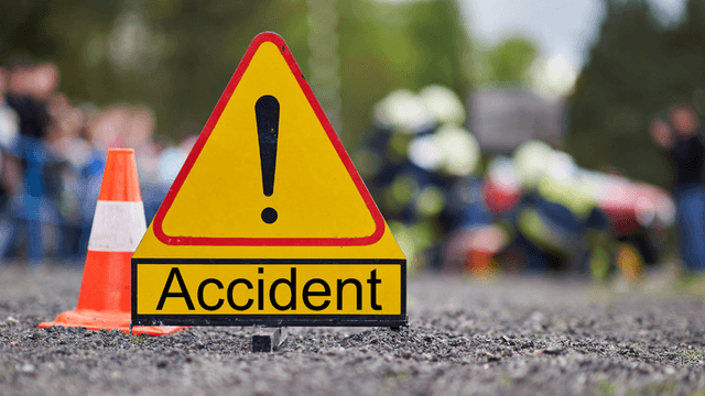 Yellow caution sign indicating an accident with blurred emergency responders in the background
