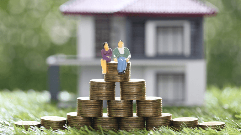 Miniature figures sit on stacks of coins in front of a house model