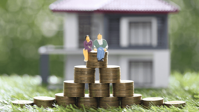 Miniature figures sit on stacks of coins in front of a house model
