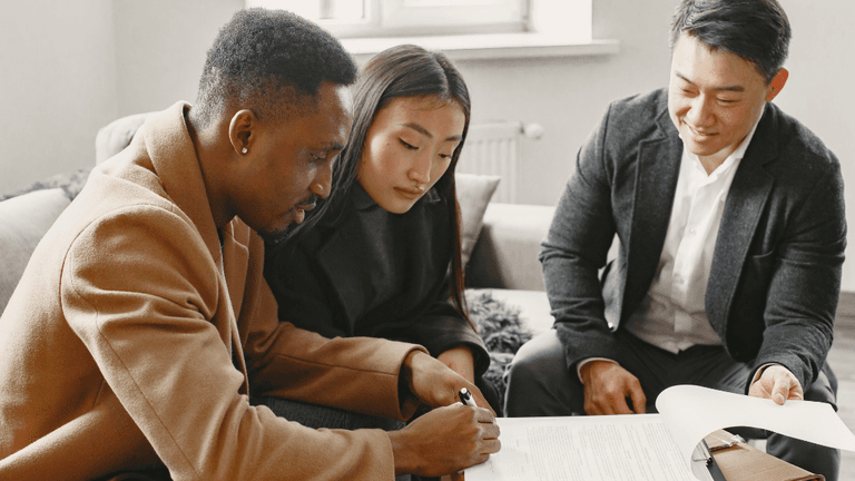 Three people reviewing and signing documents in a cozy indoor setting