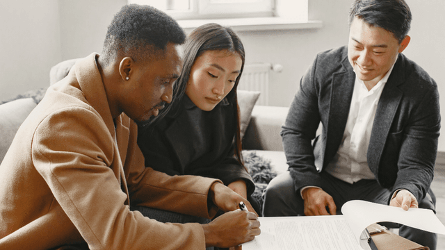 Three people reviewing and signing documents in a cozy indoor setting