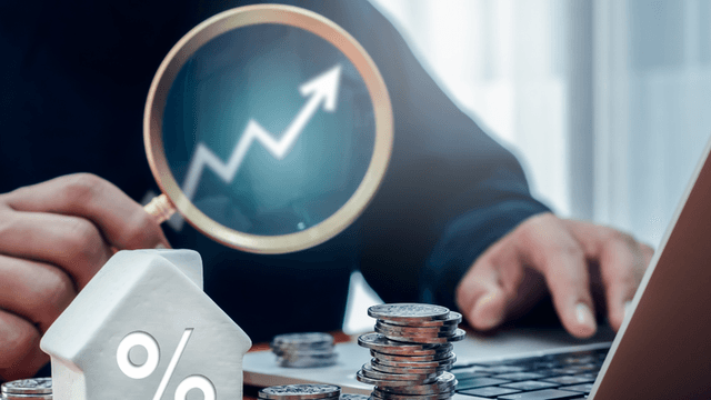 Person examining a rising graph with a magnifying glass, coins and a house figure nearby