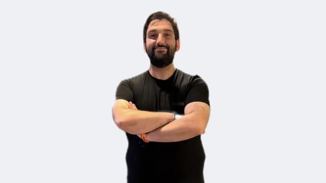 Man with crossed arms smiling, wearing a black shirt against a light background