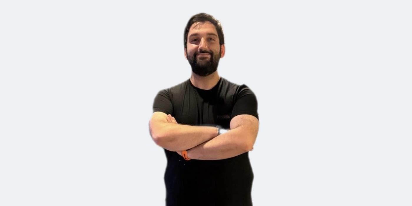 Man with crossed arms smiling, wearing a black shirt against a light background