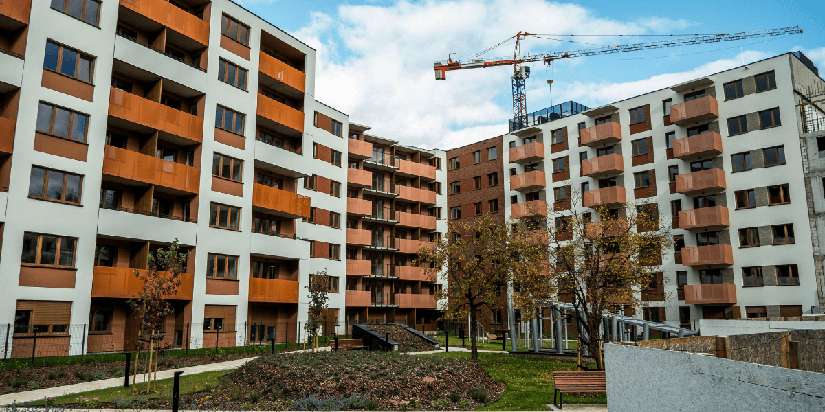 Modern apartment buildings with landscaped courtyard and construction crane in the background.