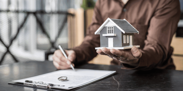 Apartment Market Shows Signs of Rebalancing as Demand Outpaces New Supply Person holding a model house while signing real estate paperwork at a desk.