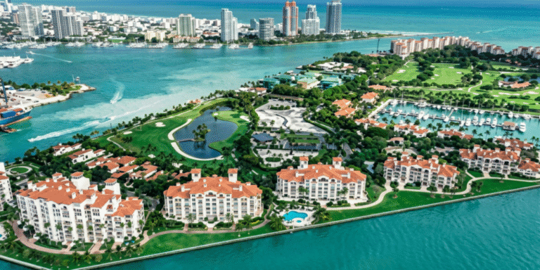 Fisher Island Loses Title as America’s Most Expensive ZIP Code, Reflecting Shifts in the Luxury Housing Market Aerial view of waterfront residences, golf courses, marina, and surrounding turquoise waters on Fisher Island.